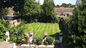 Een achtertuin met een verzorgd gazon, een kleine tuin met planten en een vogelbad, en een witte hek.