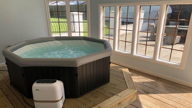 Een bubbelbad in een kamer met grote ramen, een houten terras en een kleine verwarming.
