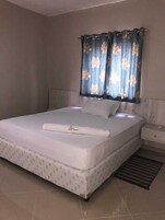 Un dormitorio con una cama grande, una mesita de noche y una ventana con cortinas florales.