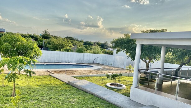 Un espacio exterior moderno con piscina, césped y un edificio blanco con balcón de vidrio.