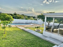 Un espacio exterior moderno con piscina, césped y un edificio blanco con balcón de vidrio.