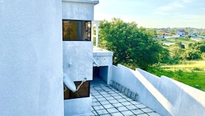 Un edificio moderno con fachada blanca, un pequeño balcón con suelo de baldosas y vistas a un paisaje verde.
