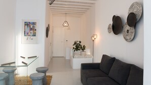 A modern living room with a grey sofa, a glass coffee table, and a minimalist design. There are decorative plates on the wall and a framed abstract painting. - Traditional Cycladic Home with a large private pool with sea view (Mikonos)