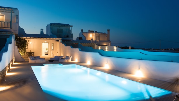A modern pool area with a clear view of the surrounding architecture, including a building with a balcony and a well-lit entrance. - Traditional Cycladic Home with a large private pool with sea view (Mikonos)