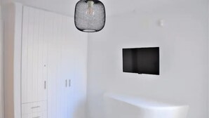 A minimalist room with a white wardrobe, a white bench, and a black TV mounted on the wall. - Traditional Cycladic Home with a large private pool with sea view (Mikonos)