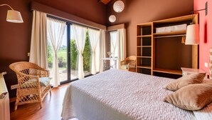A bedroom with a large bed, wicker chairs, a wooden wardrobe, and a view of greenery outside. - Apto. 3. La mar salada (Castiello De La Marina)