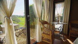 A room with wicker chairs, a table, and a view of a green landscape through a glass door. - Apto. 3. La mar salada (Castiello De La Marina)