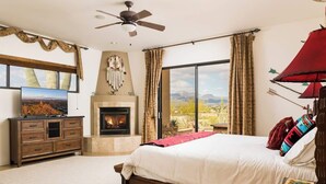A bedroom with a bed, a fireplace, a television, and a view of the outdoors. - Southwest home w/ Hot Tub, heated* pool, and amazing Mtn. Views! (Cave Creek)