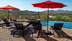 A poolside area with lounge chairs and red umbrellas, a hot tub, and a view of mountains. - Southwest home w/ Hot Tub, heated* pool, and amazing Mtn. Views! (Cave Creek)