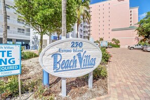 Un panneau indiquant l’emplacement des 250 villas de l’Estero Island Beach, offrant une vue dégagée sur les bâtiments environnants et les voitures garées.