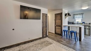 A modern kitchen with a central island, two blue bar stools, and a decorative cow head on the wall. - Cottage w/ Patio & Grill - 25 Min to Taos Valley! (El Prado)