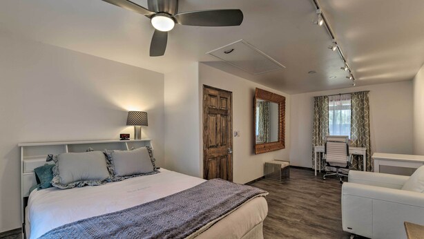 A hotel room with a bed, a desk, a chair, a ceiling fan, and a mirror. - Cottage w/ Patio & Grill - 25 Min to Taos Valley! (El Prado)