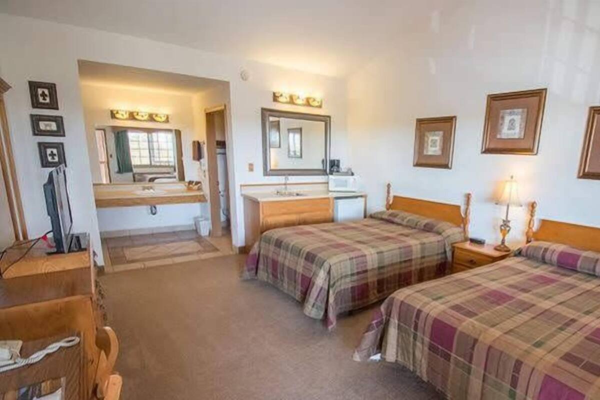 Ein Hotelzimmer mit zwei Betten, einem Schreibtisch, einem Stuhl, einem Spiegel und einem kleinen Tisch mit einer Lampe.