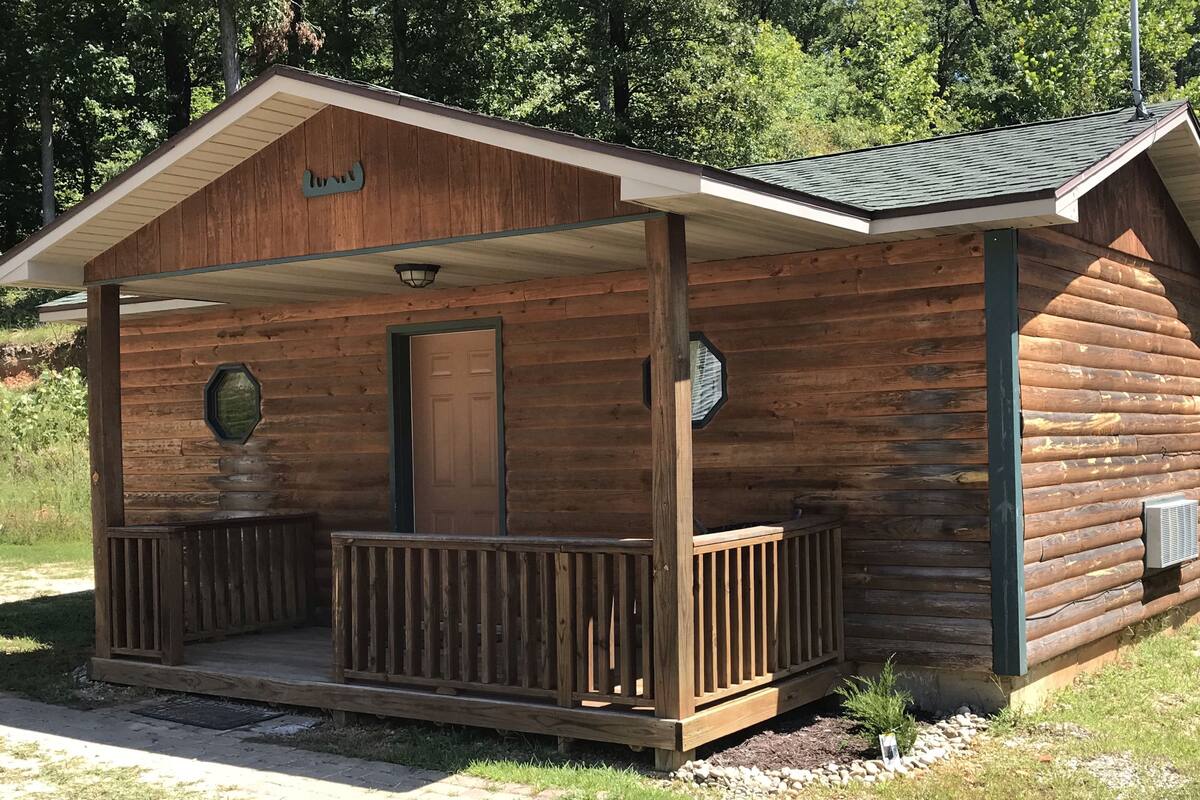Eine Blockhütte mit Veranda, einer Tür und einem kleinen Fenster.