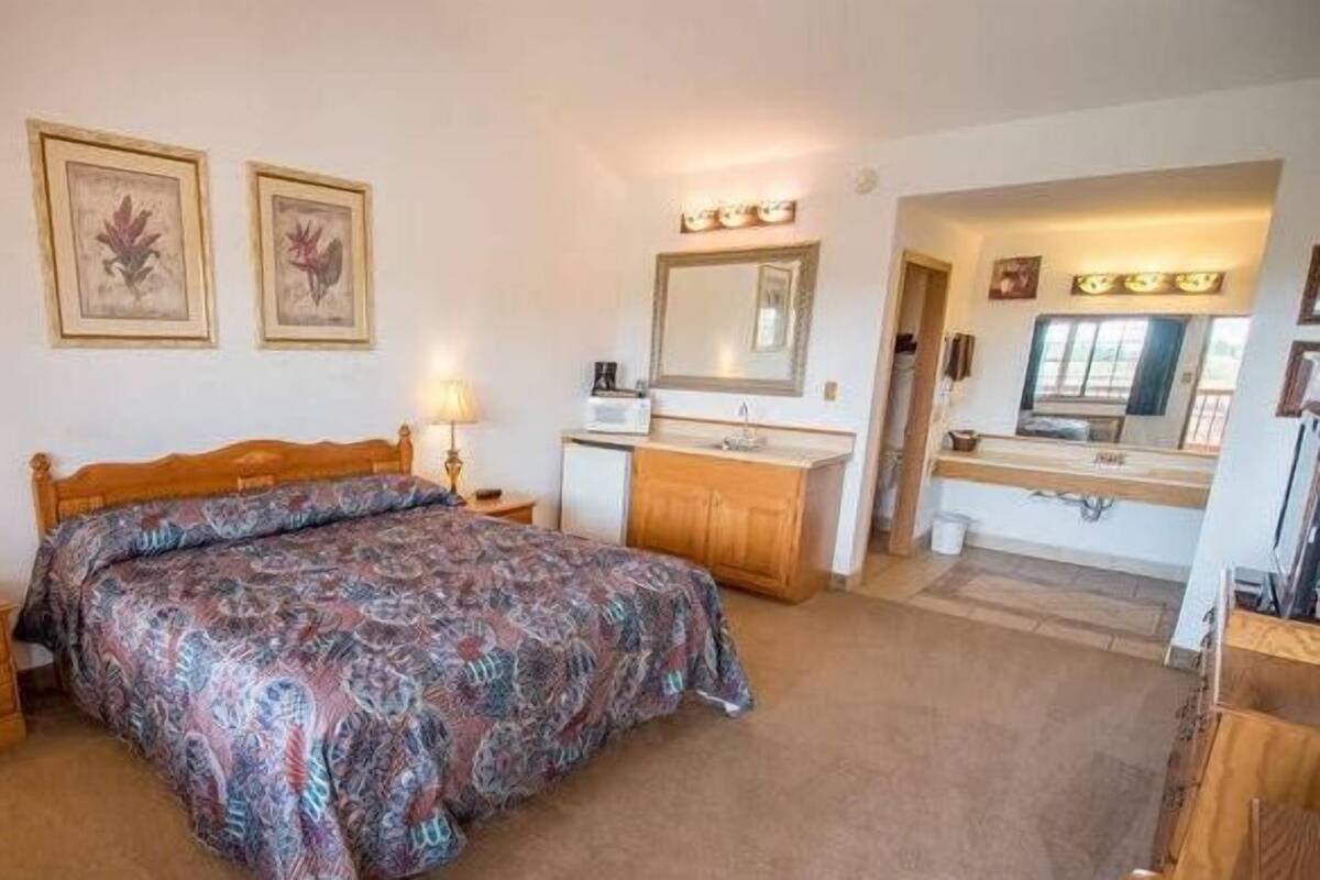 Ein Schlafzimmer mit Bett, Nachttischen, einem Schminktisch und einem Spiegel, sowie ein Badezimmer mit Waschbecken und Spiegel.