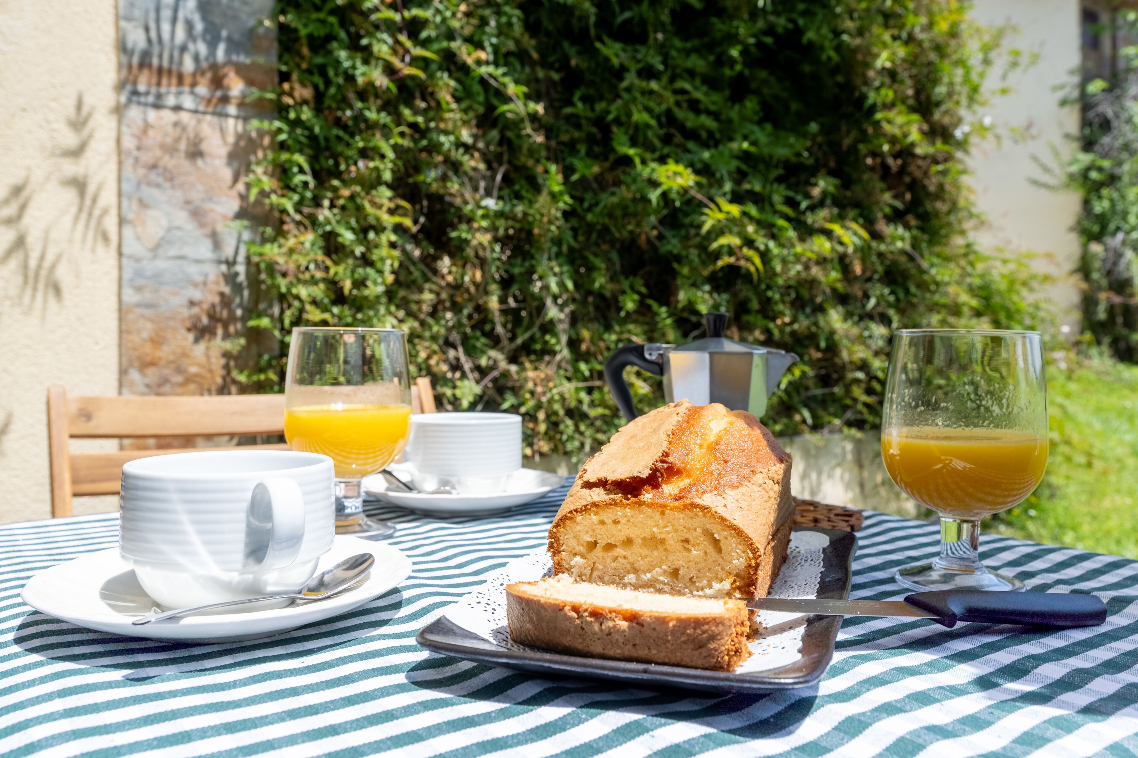 A table with a slice of cake, a glass of orange juice, and a cup of coffee on a striped tablecloth.