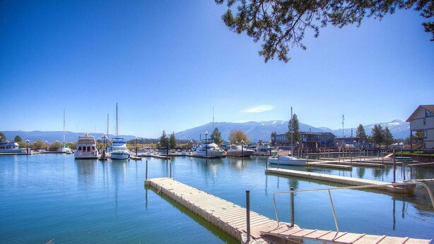 Uma marina com barcos atracados, um cais de madeira e uma montanha ao fundo.