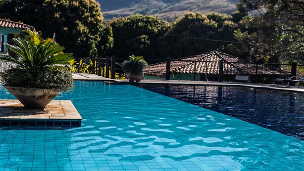 Una piscina con suelo de baldosas, rodeada de plantas en macetas y una pérgola.