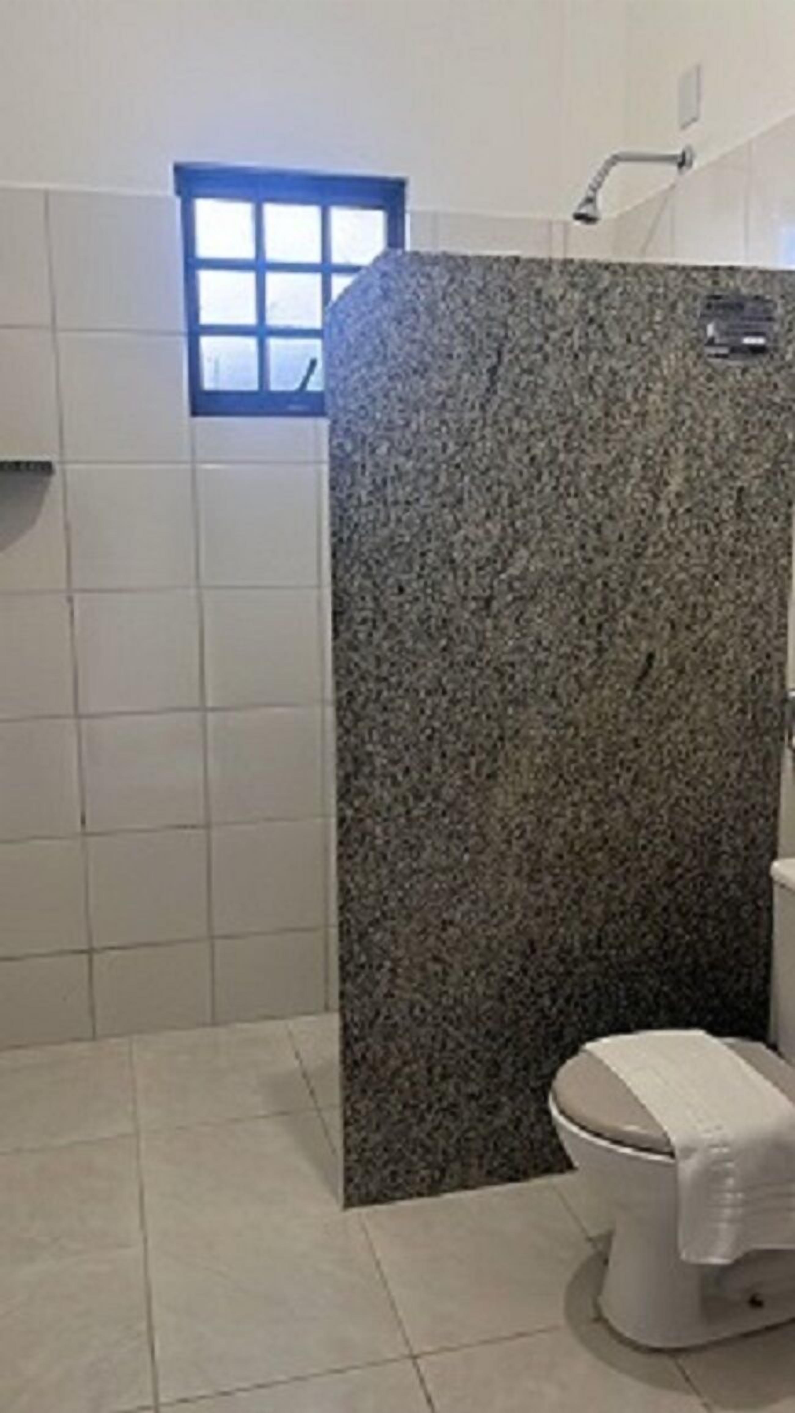 A bathroom with a granite shower enclosure, a toilet, and a window.