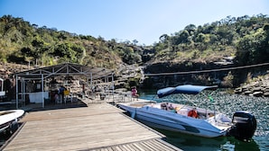 Un muelle de madera con una zona de estar cubierta, un bote y un promontorio rocoso al fondo.