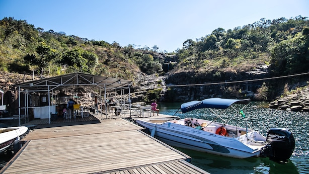 Une jetée en bois avec un espace de repos abrité, un bateau et, au loin, une colline rocheuse.