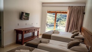 Habitación de hotel con dos camas, un escritorio de madera, televisor y un ventanal con cortinas.