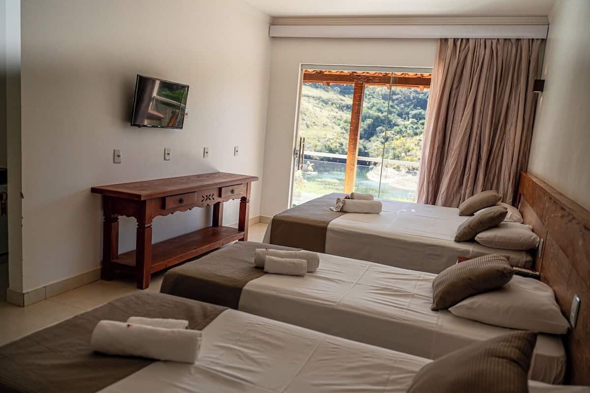 Habitación de hotel con dos camas, un escritorio de madera, televisor y un ventanal con cortinas.