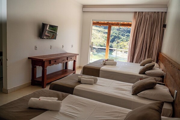 A hotel room with two beds, a wooden desk, a TV, and a large window with curtains. - Pousada do Rio Turvo (Capitólio)