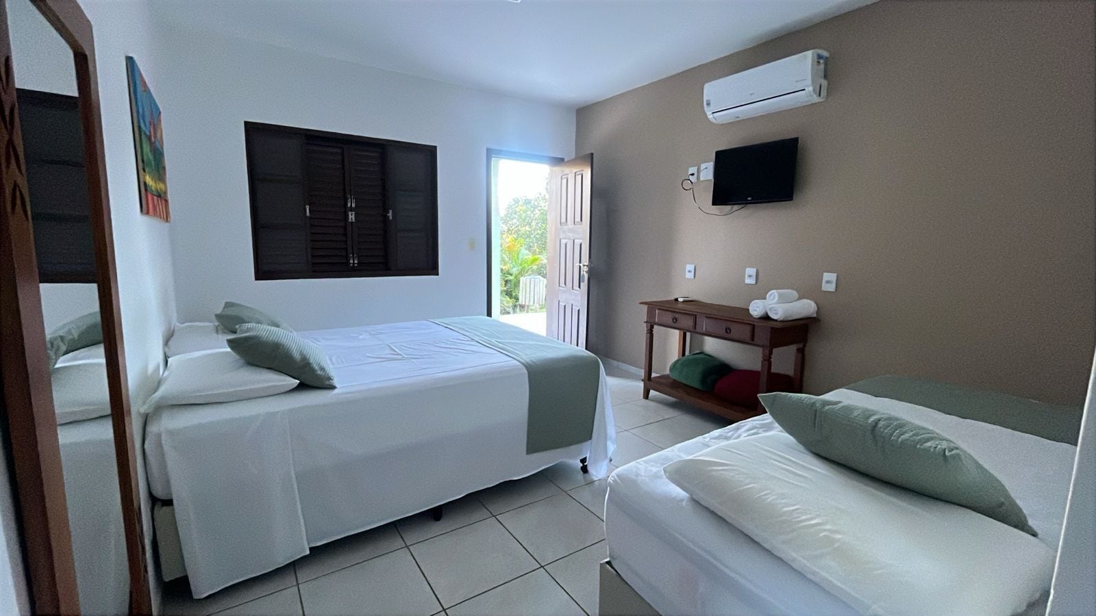 A hotel room with two beds, a TV, an air conditioner, and a small table with towels.