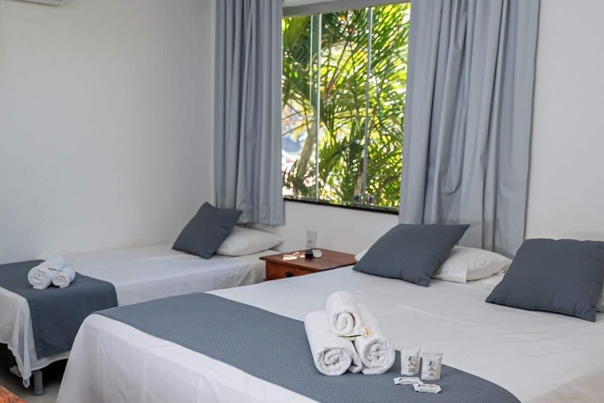 Habitación de hotel con dos camas, una ventana con cortinas, una mesita de noche y aire acondicionado instalado en la pared.