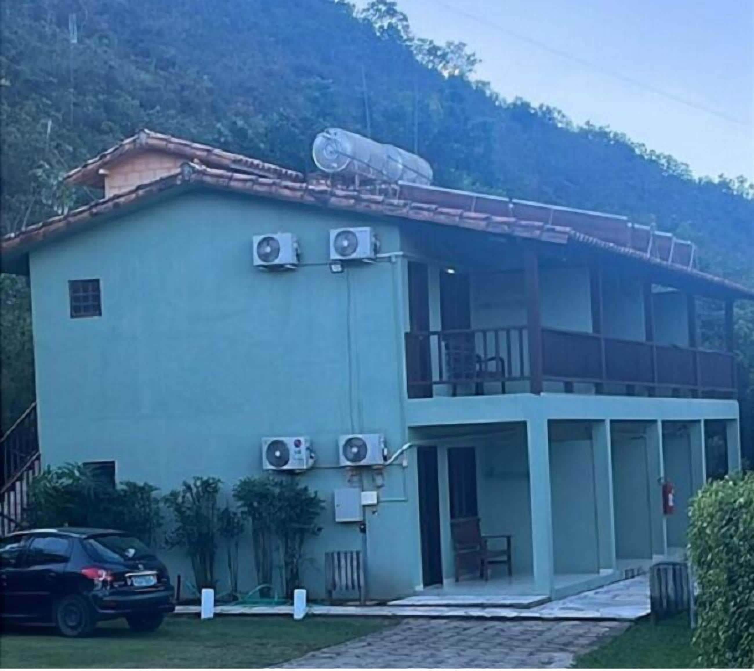 A two-story building with a flat roof, air conditioning units, a satellite dish, and a car parked in front.