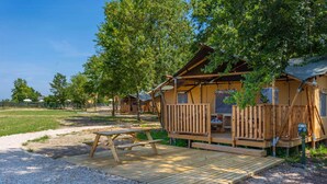 Une cabane en bois dotée d’une terrasse et d’une table de pique-nique, entourée d’arbres et bordée d’un chemin de gravier.