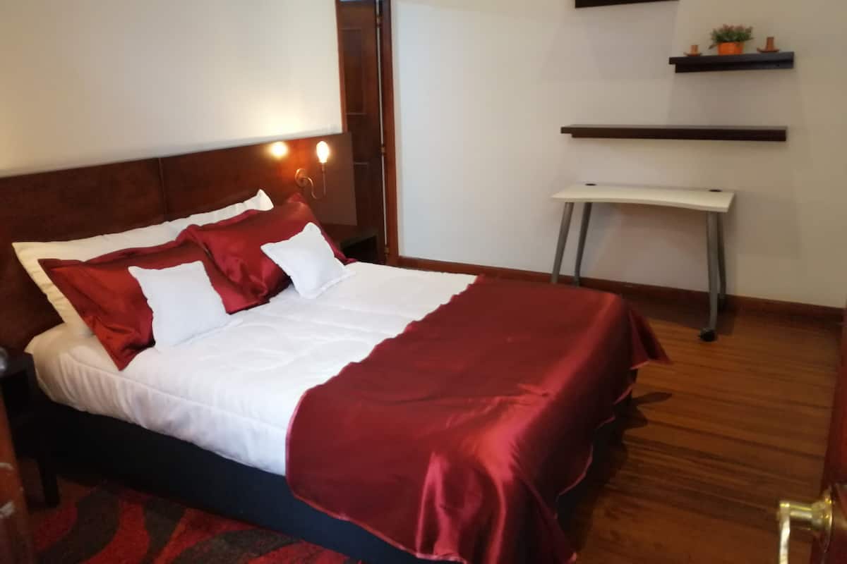 Ein ordentlich bezogenes Bett mit roter und weißer Bettwäsche, ein Nachttisch und eine kleine Ablagefläche mit Dekoration.