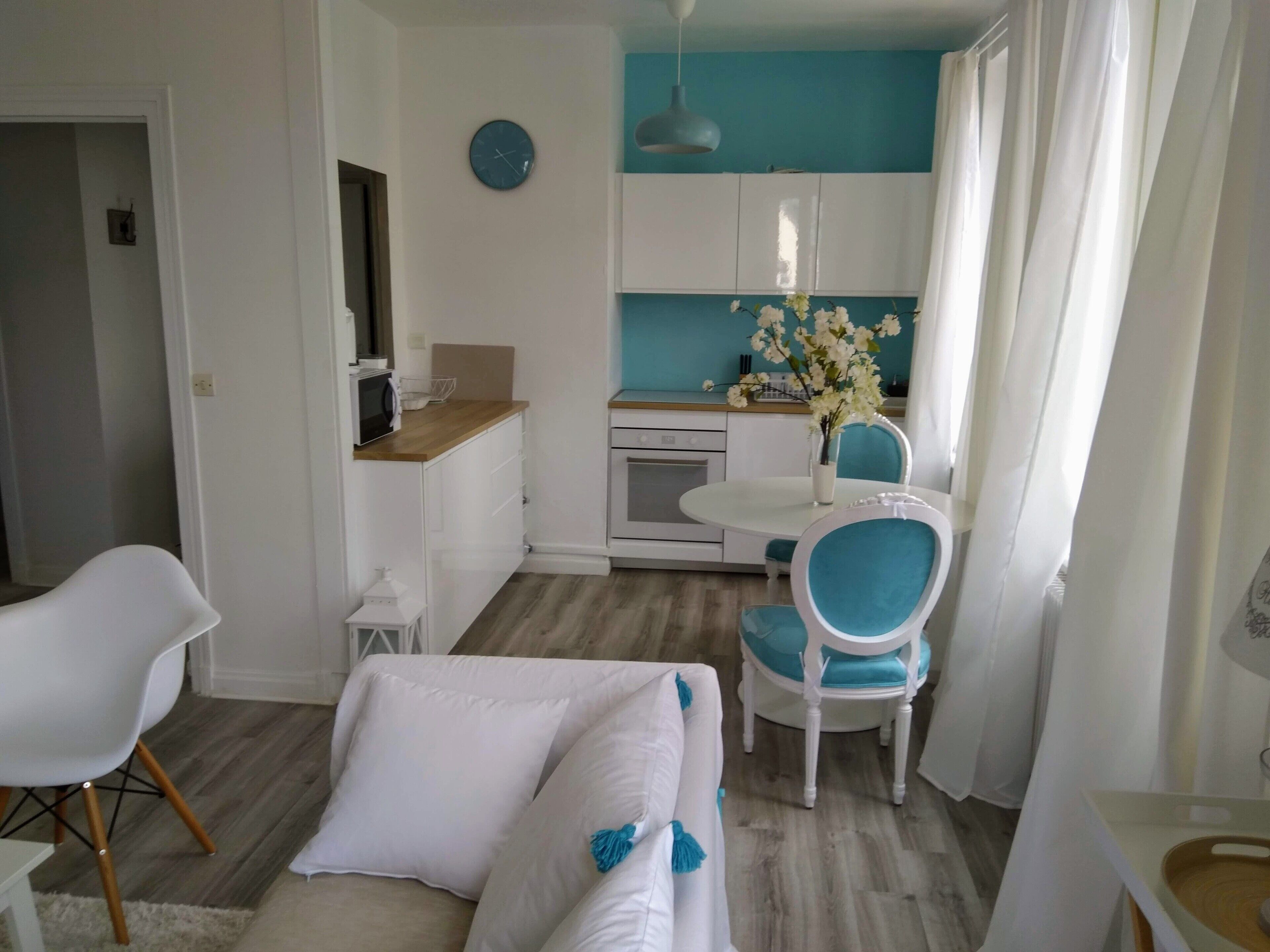 A modern kitchen with white cabinets, a blue accent wall, and a dining area with white and blue chairs.