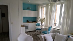 Uma sala de estar moderna com sofá, uma mesa de jantar com cadeiras, área de cozinha com armários e uma janela grande com cortinas.