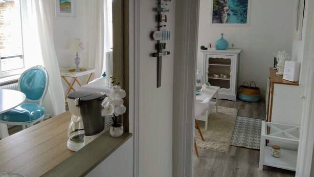 Uma cozinha moderna com área de refeições, apresentando uma cafeteira, um vaso com flores brancas e um armário com objetos decorativos.