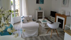 Uma sala de estar moderna com um sofá branco, uma mesa de centro, uma TV e uma lareira.