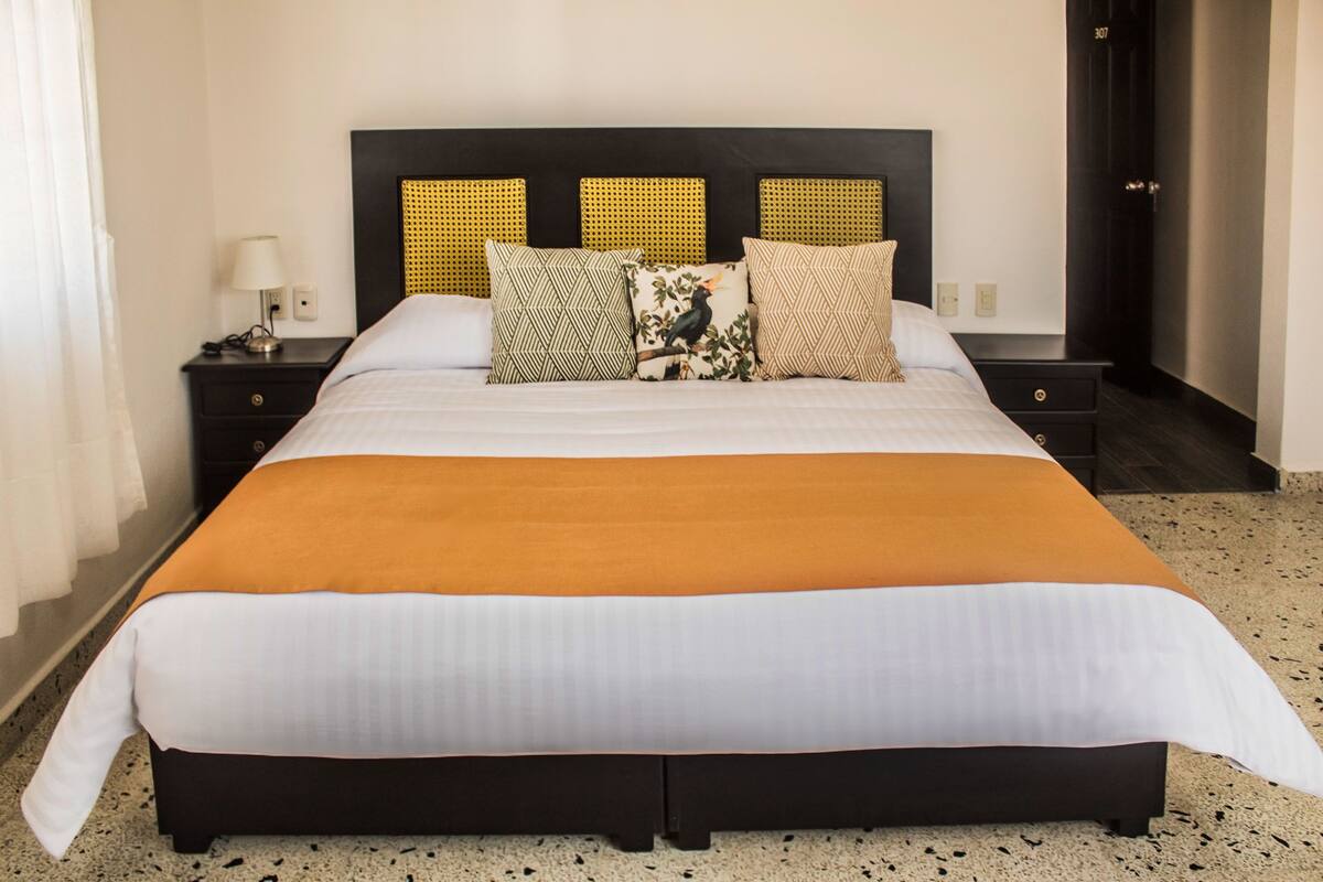 A hotel room with a large bed, a nightstand with a lamp, and a door with the number 307.