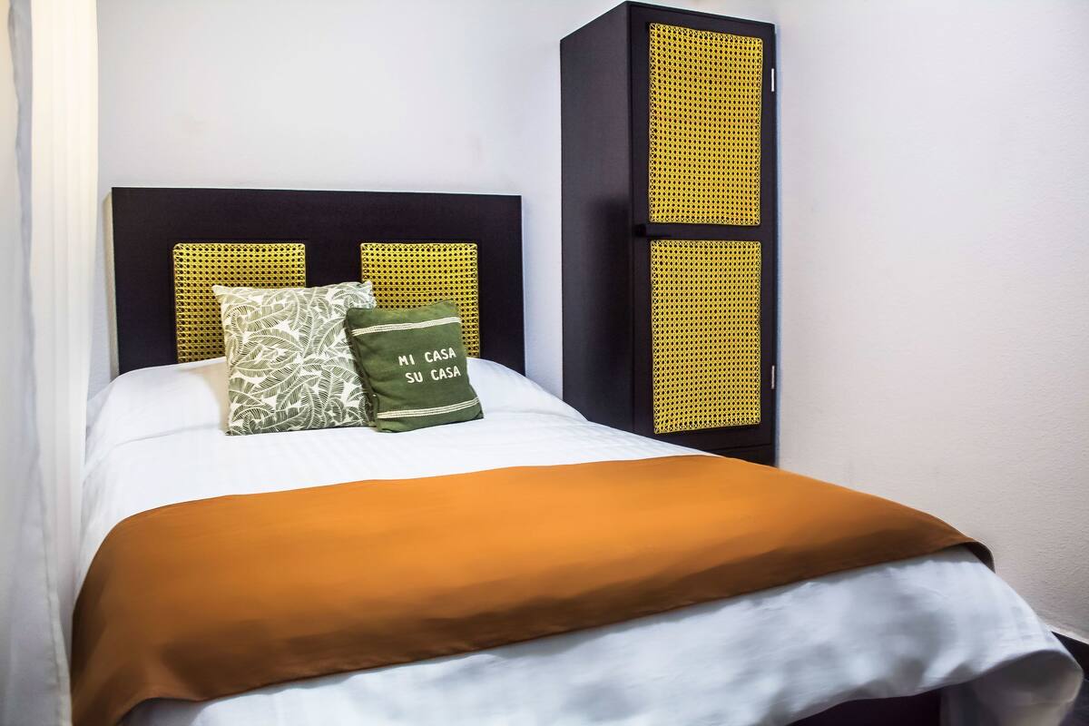 A bed with a white mattress, a brown blanket, and two pillows with text.