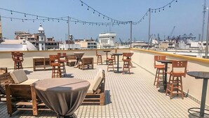 A rooftop terrace with wooden furniture, string lights, and a view of the cityscape. - Hotel Múcara (Veracruz)