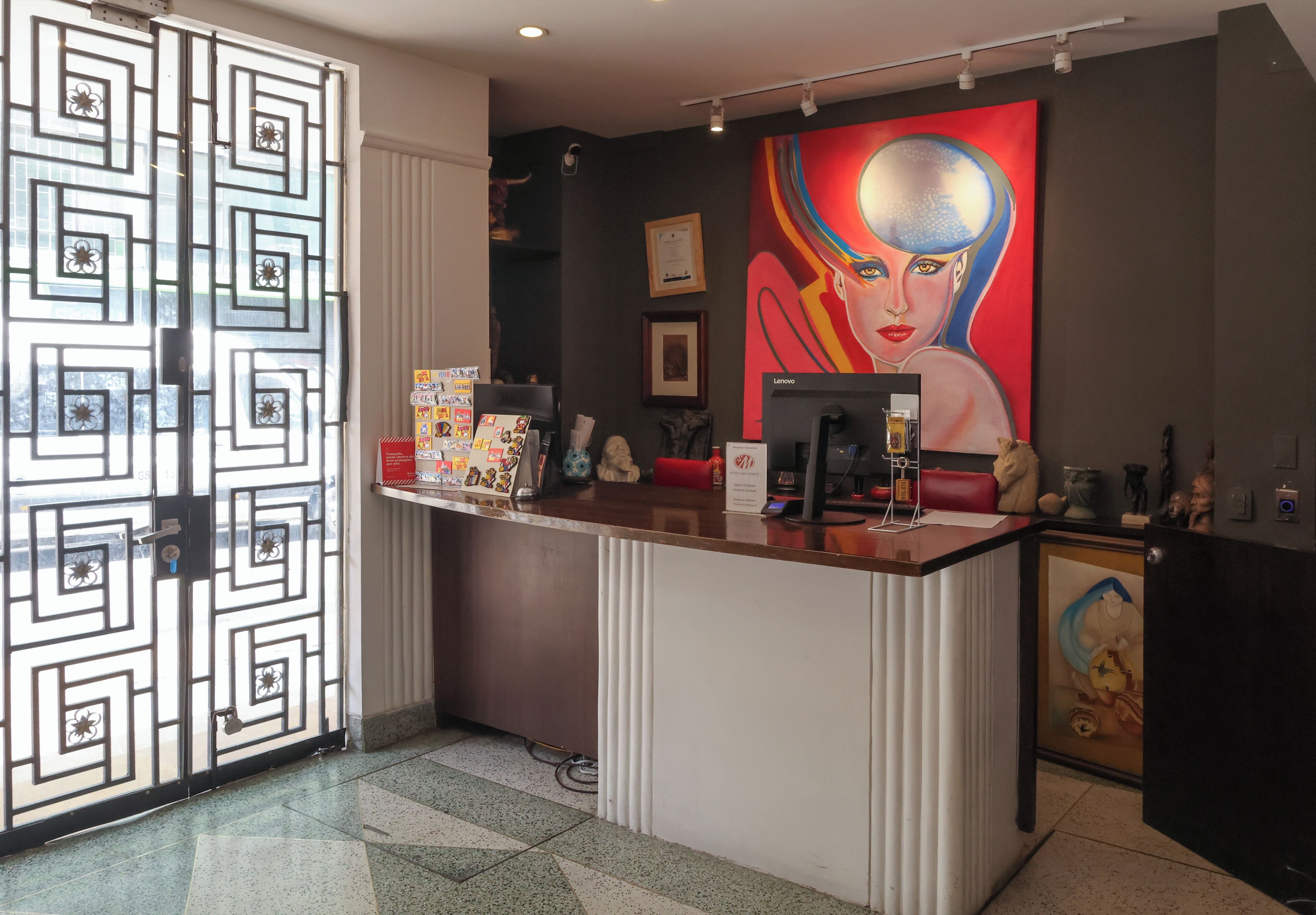 Un comptoir d’accueil équipé d’un ordinateur, agrémenté d’œuvres d’art encadrées et d’une porte décorative.