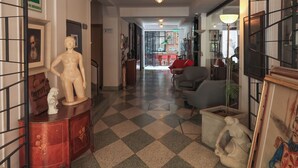 A hallway with a checkered floor, a statue, a mannequin, and a red sofa. - Hotel Museo San Moritz (Bogotá)