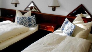 A hotel room with two beds, each with white linens and blue patterned pillows. There are wooden headboards, bedside tables, and wall-mounted lamps. - Hotel Froschkönig (Kassel)