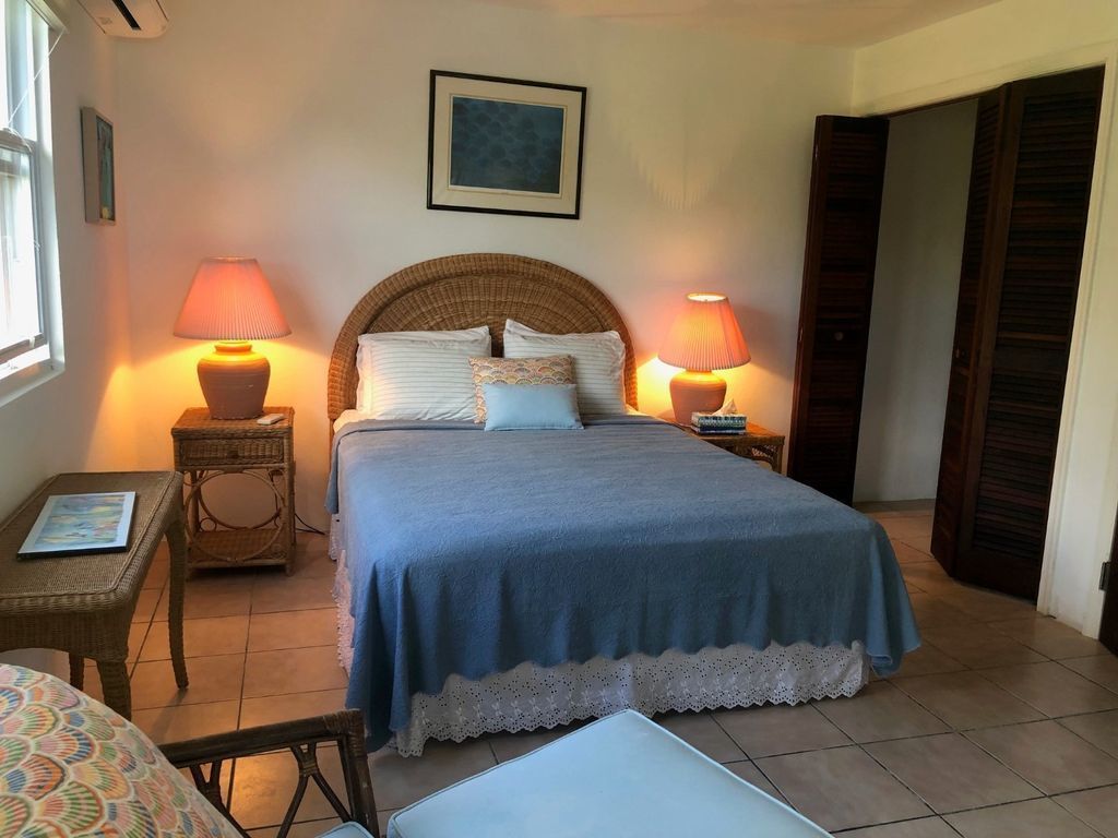 Ein Schlafzimmer mit einem Bett, zwei Nachttischlampen, einem Korbstuhl, einem Sessel und einem gerahmten Bild an der Wand.