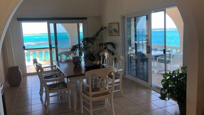 A dining area with a view of the ocean, white chairs, a table, and a ceiling fan. - Patricks Bay Villa (Island Harbour)