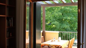 Ein Zimmer mit einem Bett, einem Bücherregal und einem Essbereich mit Tisch und Stühlen. Eine Glastür öffnet sich zu einer Außenpatio mit Tisch und Stühlen.