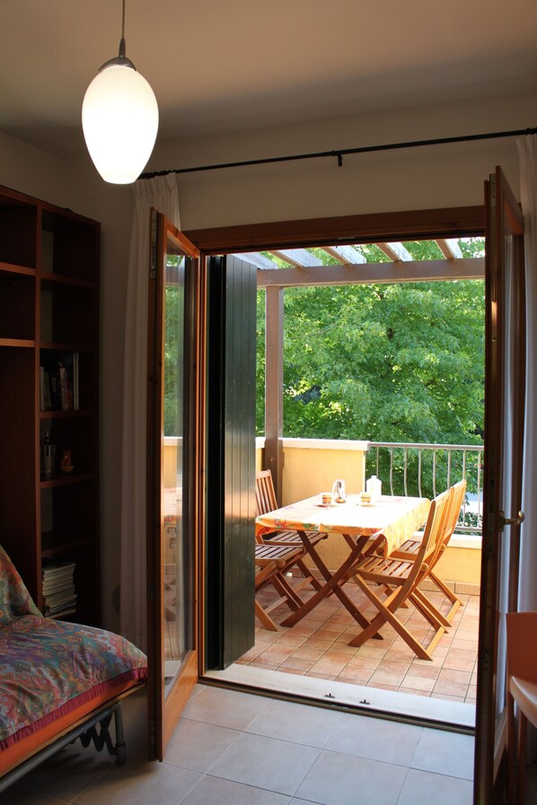 Una stanza con un letto, una libreria e un'area pranzo con tavolo e sedie. C'è una porta finestra scorrevole che dà su un patio esterno con tavolo e sedie.