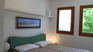 Ein Schlafzimmer mit einem Bett, einem gerahmten Bild an der Wand, einem Fenster und einem Regal mit einer Vase.