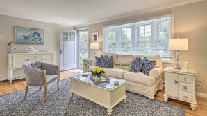 A living room with a beige sofa, a gray armchair, a glass coffee table with a floral centerpiece, and a white sideboard with starfish decorations. - ~ 4 Mi to Dtwn: Chatham Home w/ Fire Pit (South Chatham)