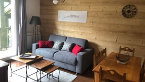 A cozy living room with a grey sofa, red and white cushions, a wooden dining table, and a black floor lamp. - Cozy 2BR apt for 6 in Peyragudes with ski access (Peyragudes)